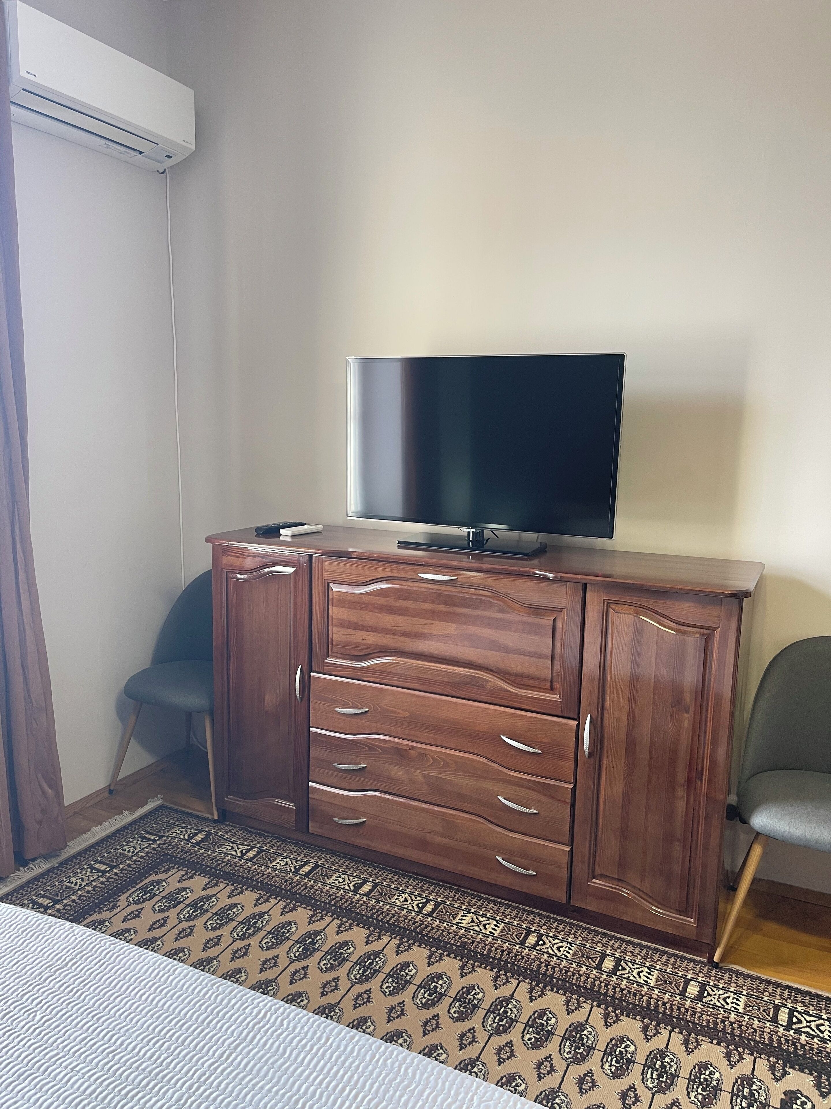 Una habitación con un armario de madera, un televisor de pantalla plana, un tapete estampado y una silla.