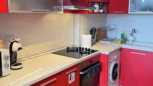 A modern kitchen with red cabinetry, a built-in stove, oven, and a washing machine. - Dara House (Plovdiv)