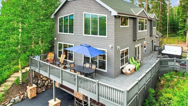 A two-story house with a deck, large windows, and a covered outdoor seating area.