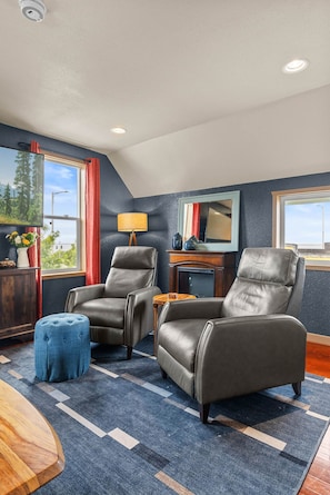 A room with two leather armchairs, a blue ottoman, a wooden side table, and a fireplace.