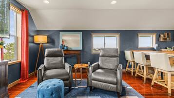 A modern living room with two leather armchairs, a coffee table, and a dining area with a wooden table and chairs.