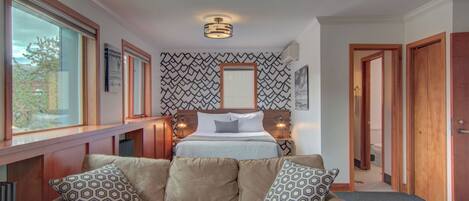 A hotel room with a bed, a sofa with patterned cushions, a window, and a patterned wall.