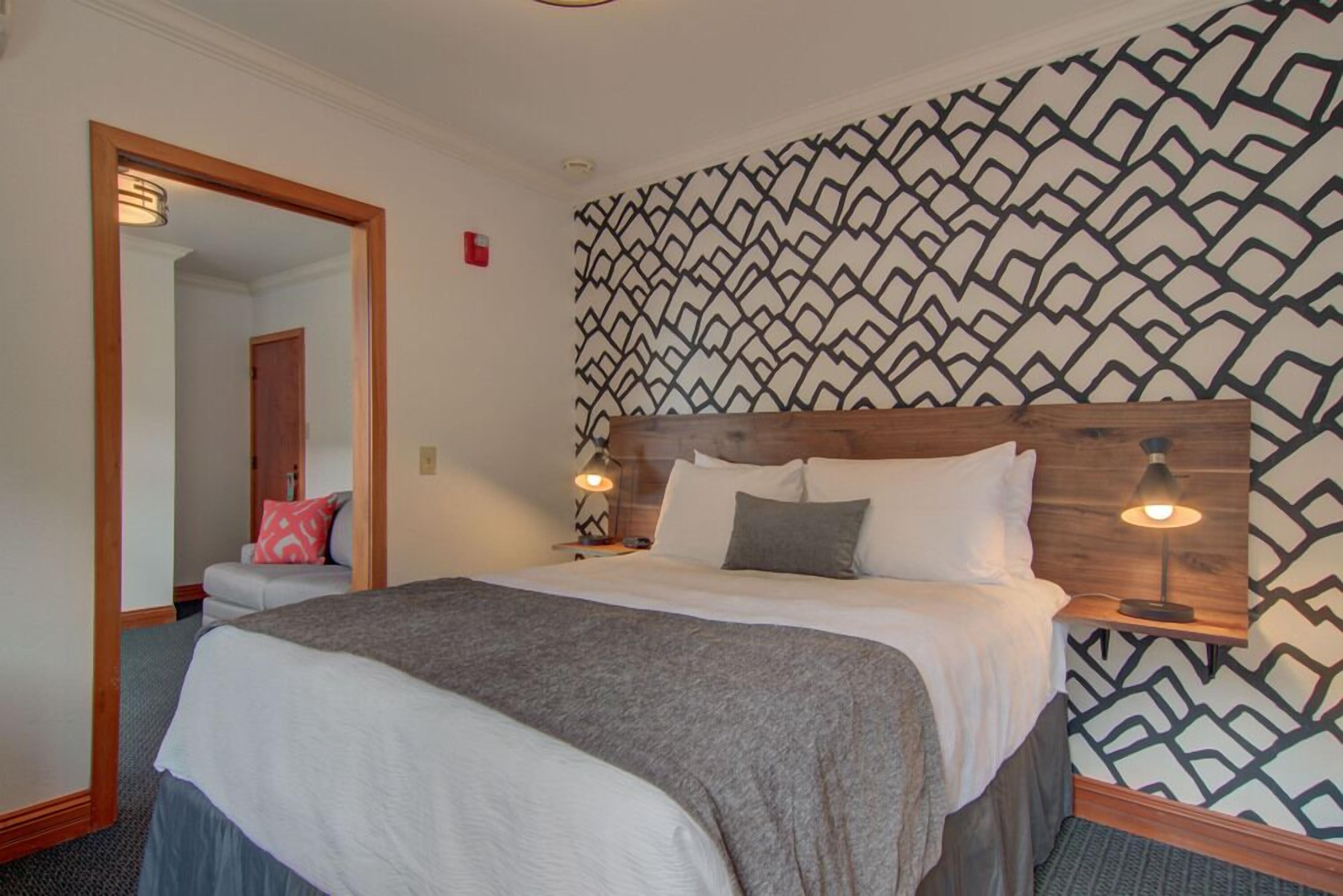 A hotel room with a bed, bedside lamps, a patterned wall, and a mirror.