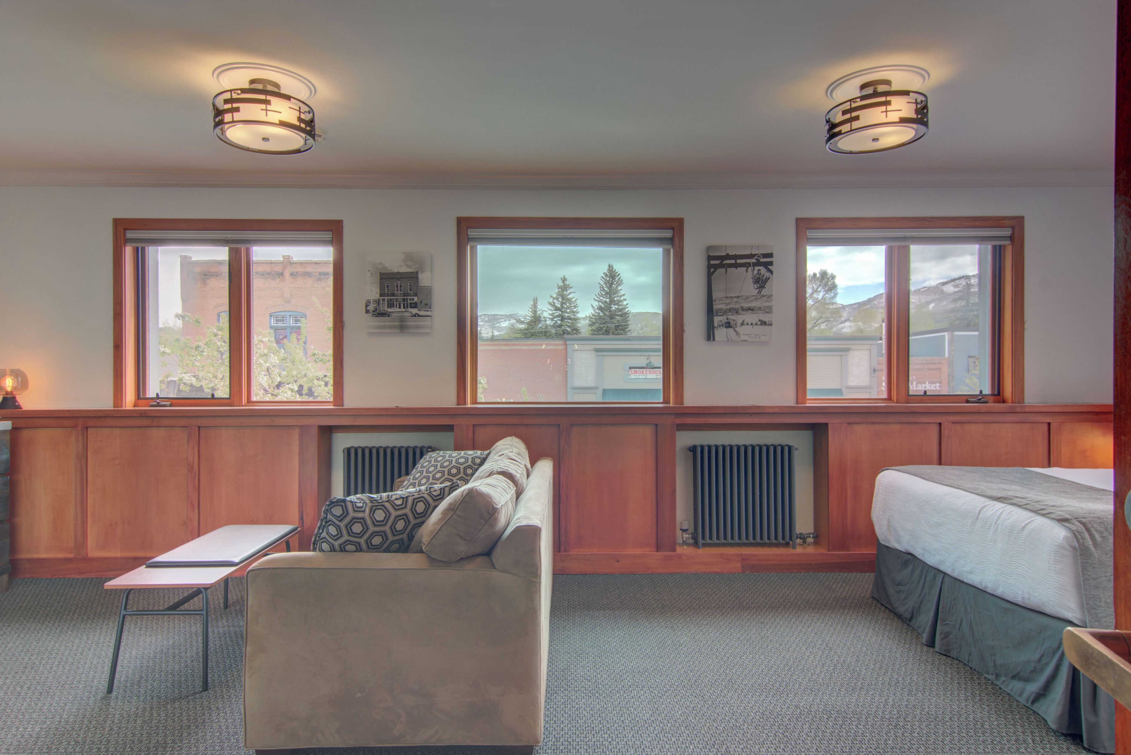 A hotel room with a large window, a sofa, a bed, and a small table.