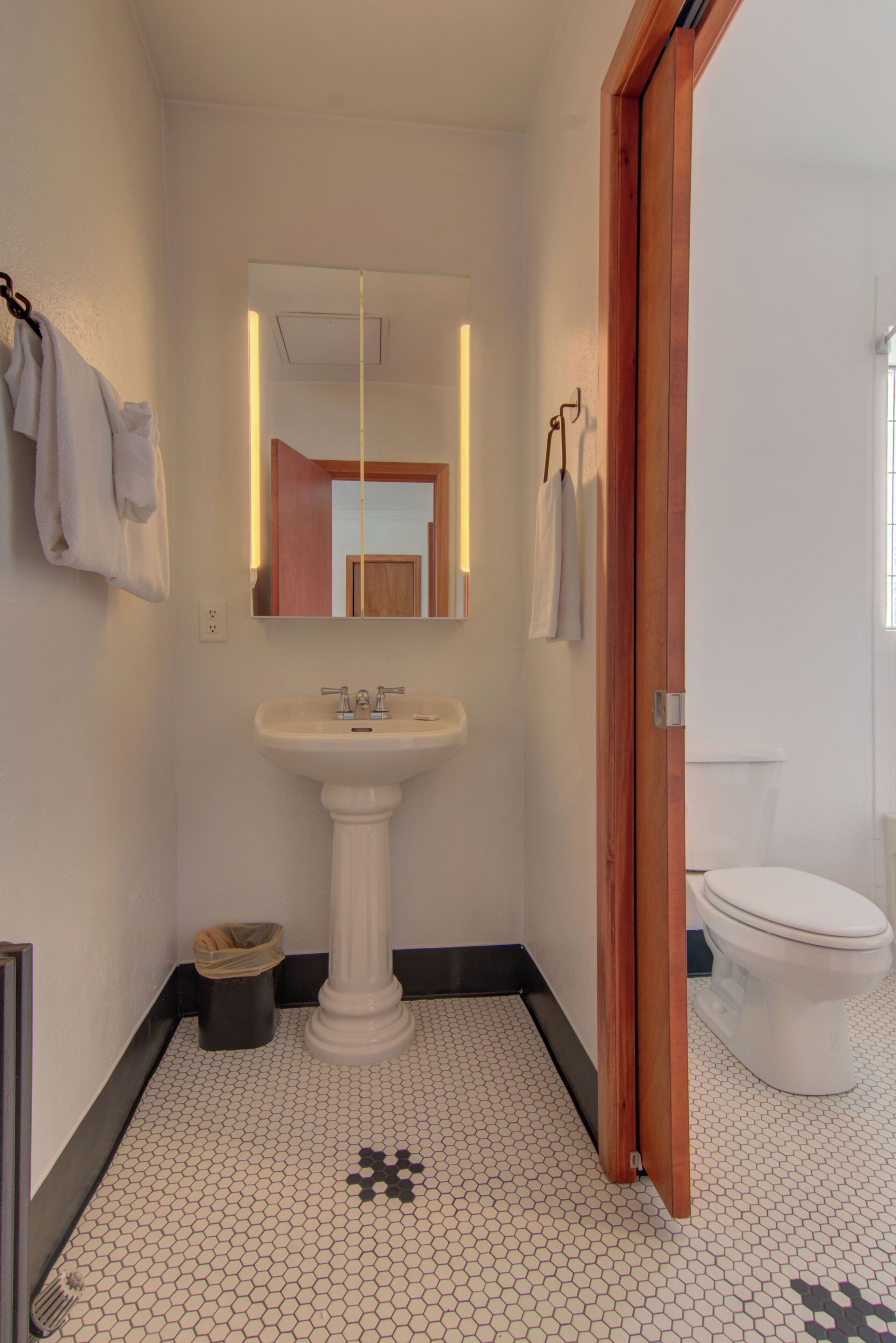 Une salle de bain avec un lavabo sur colonne, un miroir, des toilettes et un sol carrelé.
