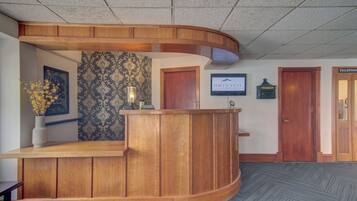 Un área de recepción con un mostrador de madera curva, un televisor montado en la pared y un papel tapiz estampado.