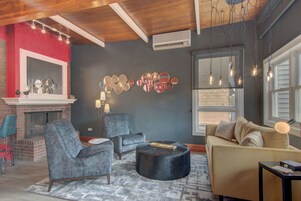 Una sala de estar con chimenea, dos sillones, un banqueta redonda, un sofá y una pared con espejos circulares.