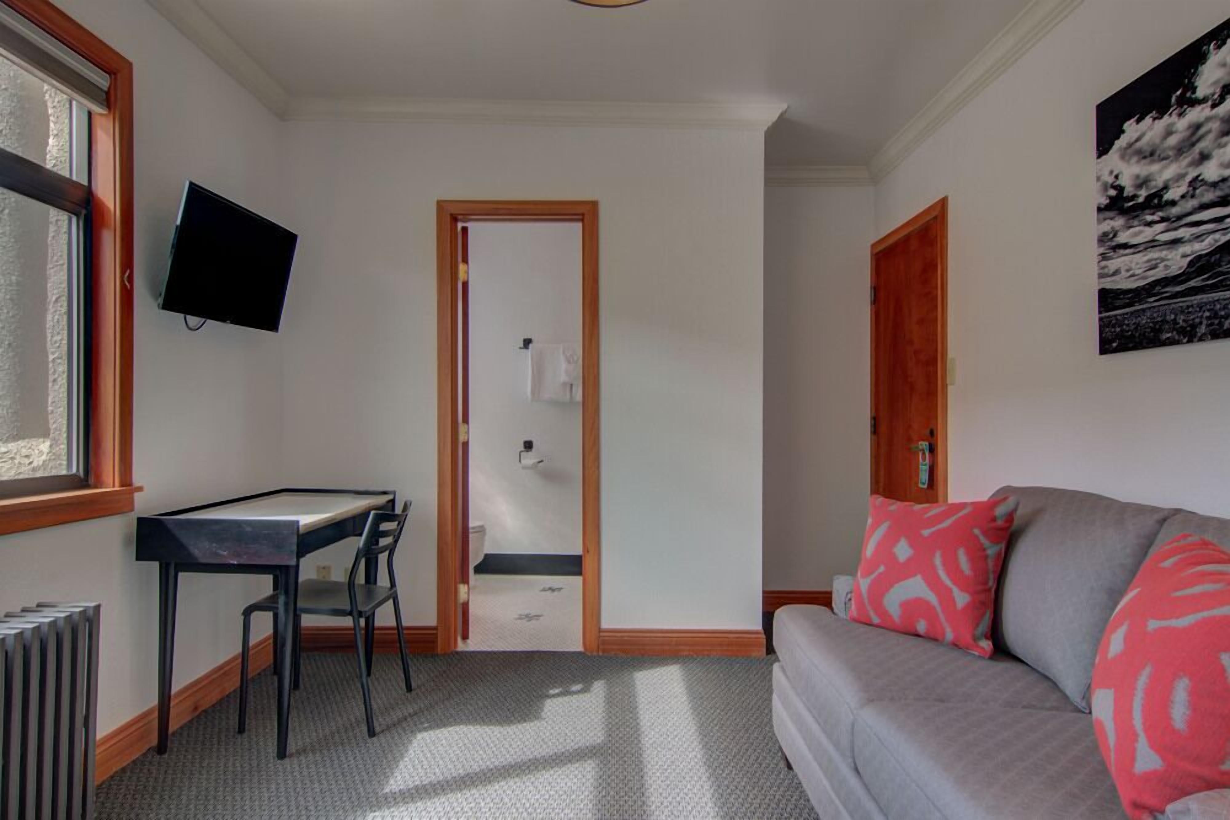 Une pièce comprenant un bureau, une chaise, un canapé, un téléviseur fixé au mur et une porte donnant accès à une salle de bain.