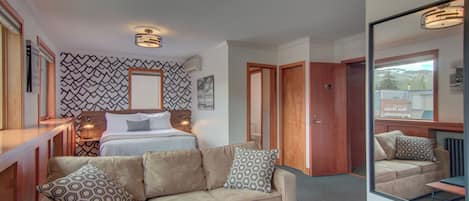 A hotel room with a bed, a sofa, a mirror, and a patterned wall.