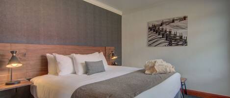 A neatly arranged hotel room with a large bed, two bedside tables with lamps, a headboard, a wall-mounted artwork, and a carpeted floor.