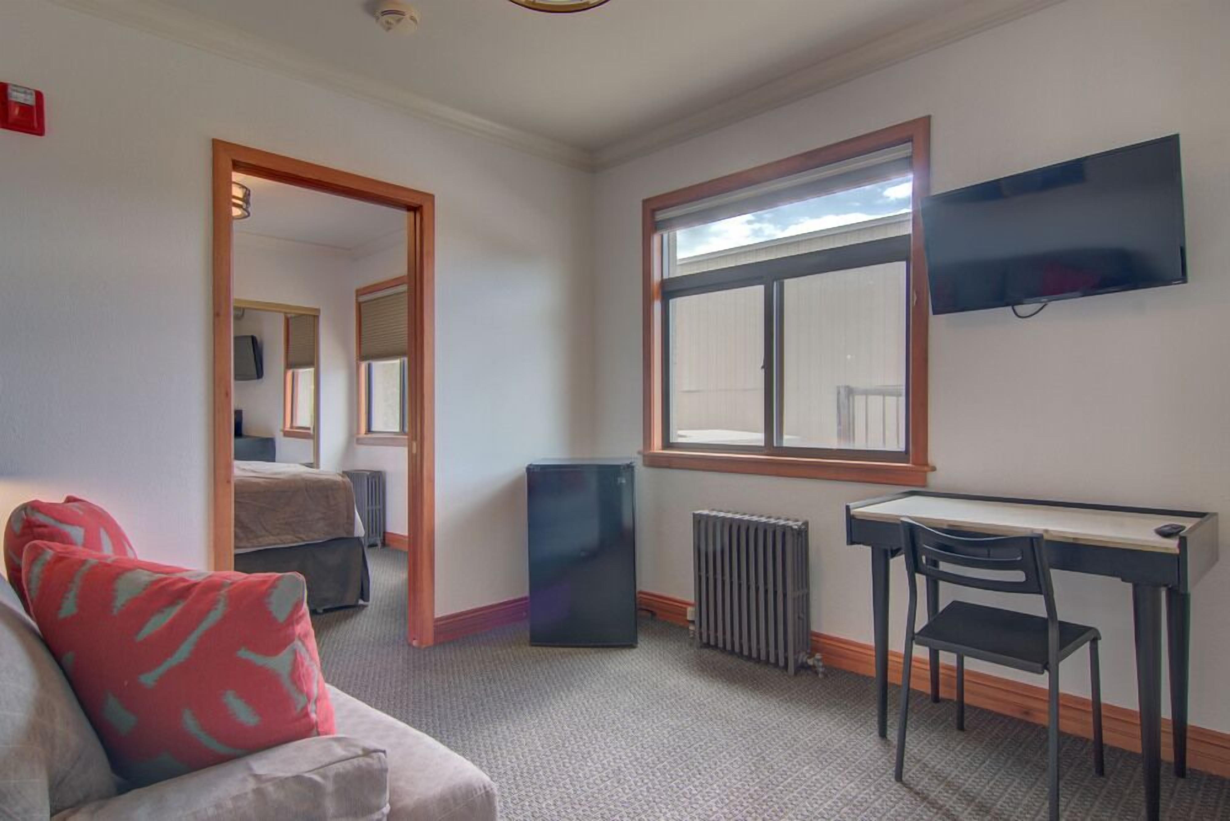 Una habitación con una cama, un escritorio, una silla, un radiador y un televisor en la pared.