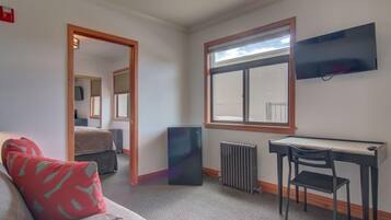 Una habitación con una cama, un escritorio, una silla, un radiador y un televisor en la pared.