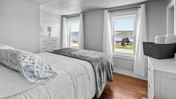 Un dormitorio con cama, mesita de noche, cómoda y ventana con vistas al mar.