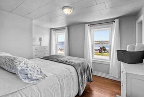 A bedroom with a bed, a nightstand, a dresser, and a window with a view of the sea. - 4 Bedroom House near Whale Watching and Mistaken Point Ecological Reserve. (Trepassey)