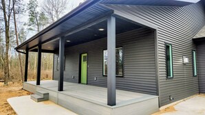 A modern house with a covered porch, large windows, and a green door.