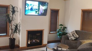 A living room with a wooden ceiling, a flat-screen TV mounted on the wall, a fireplace, and a large sectional sofa.