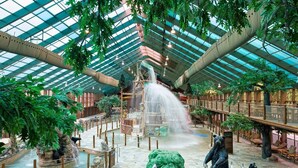Ein geräumiger Innenhof mit hoher Glasdecke, einem zentralen Wasserspiel und verschiedenen Sitzbereichen.