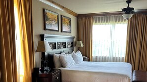Ein Hotelzimmer mit einem großen Bett, einer separaten Sitzecke, einem Badezimmer mit Badewanne und einem Deckenventilator.