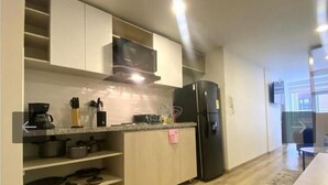 A modern kitchen with white cabinetry, a black refrigerator, and a microwave. There are pots and pans on the lower shelves, and a coffee maker on the countertop.