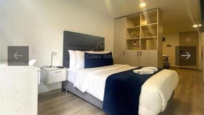 A modern hotel room with a bed, bedside table, and a wardrobe.