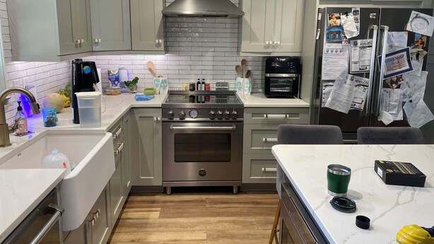 Una cocina moderna con armarios grises, estufa de acero inoxidable, horno empotrado y refrigerador cubierto de papeles.