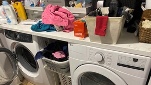 Zona de lavandería con dos lavadoras, una secadora y diversos productos de limpieza sobre una encimera.