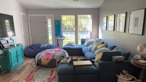 Una sala de estar con un sofá seccional azul, un tapete colorido, un mueble azul turquesa y un ventanal con vistas a la vegetación.
