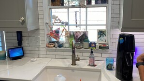 Una cocina con un lavamanos blanco, una cafetera y una ventana decorada.