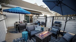 An outdoor patio area with a wooden table, two sofas, a fire pit, and a barbecue grill.