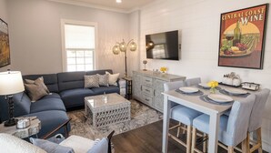 A modern living room with a sectional sofa, a dining area with bar stools, and a kitchen with a large TV.