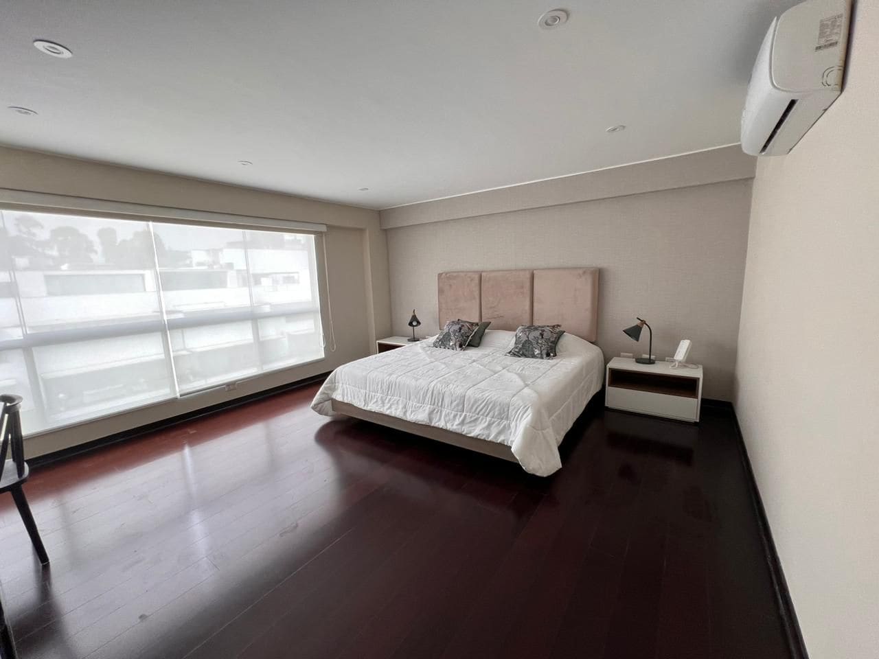 Quarto com cama grande, mesa de cabeceira, abajur e janela com persianas.
