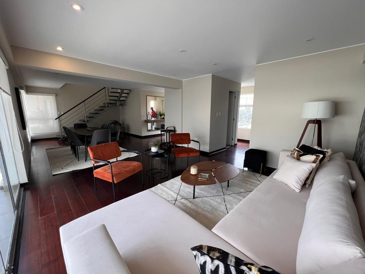 A modern living room with a sofa, coffee table, and chairs. There is a staircase leading to an upper level.