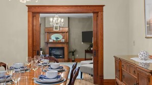 Une salle à manger avec une table à manger en bois, dressée pour le repas, une cheminée avec un manteau et un lustre.