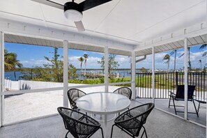 Een overdekt terras met een ronde tafel en vier stoelen, met uitzicht op een jachthaven en het water.
