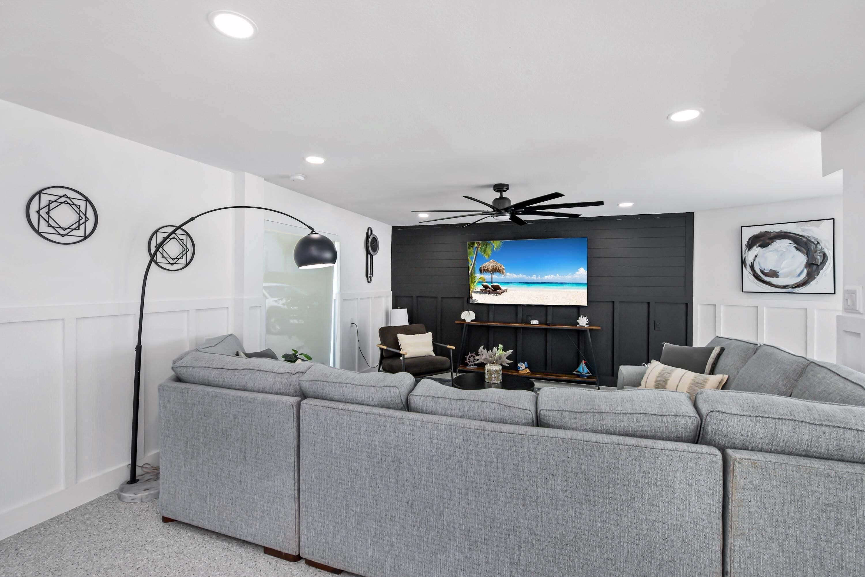 A modern living room with a sectional sofa, a ceiling fan, and a large TV screen.