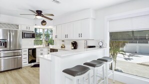 A modern kitchen with white cabinetry, stainless steel appliances, and a bar area with stools.