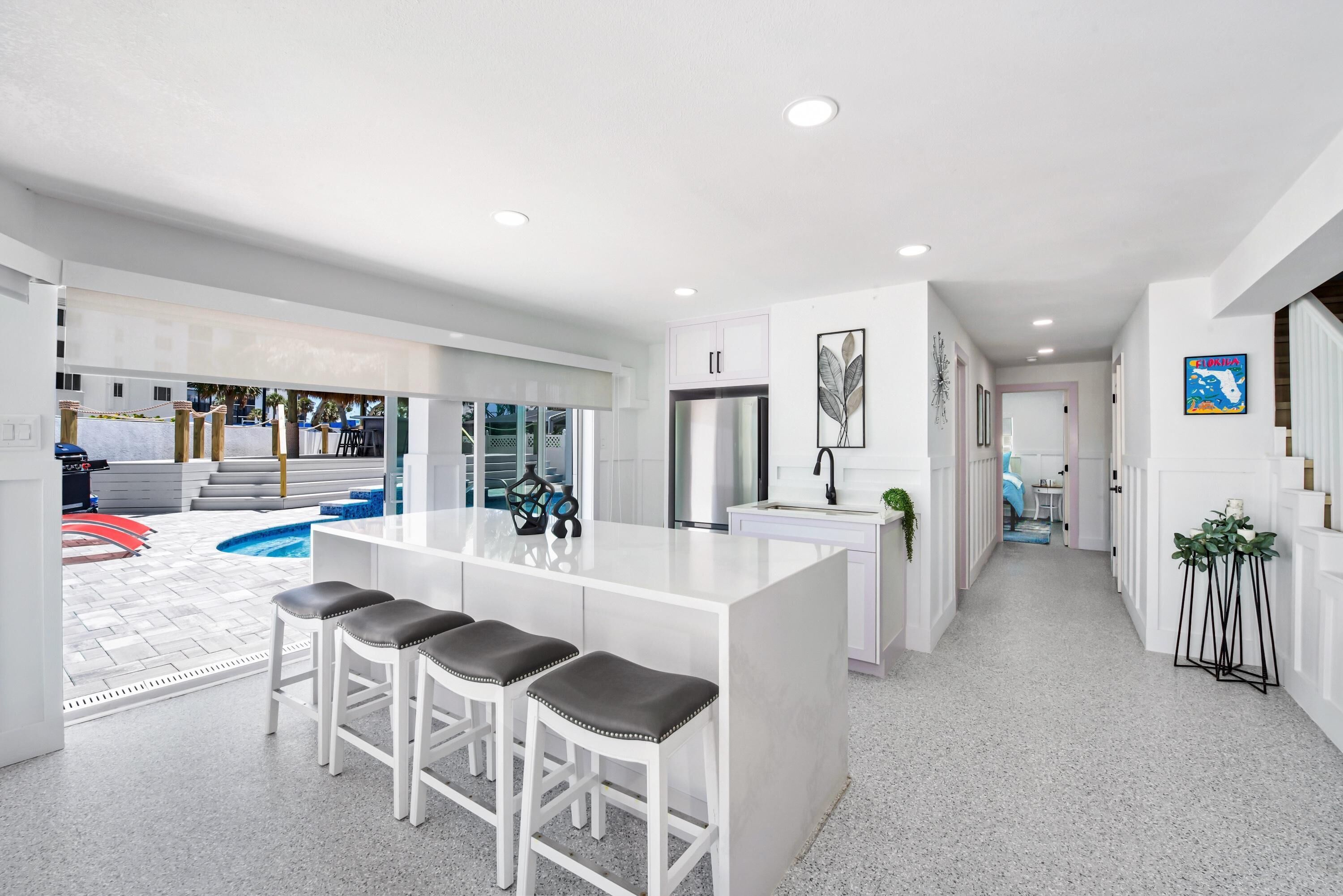 Una cocina moderna con una isla central, taburetes de bar y vistas al área de la piscina exterior.
