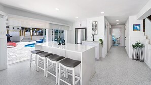 A modern kitchen with a central island, bar stools, and a view of the outdoor swimming pool area.