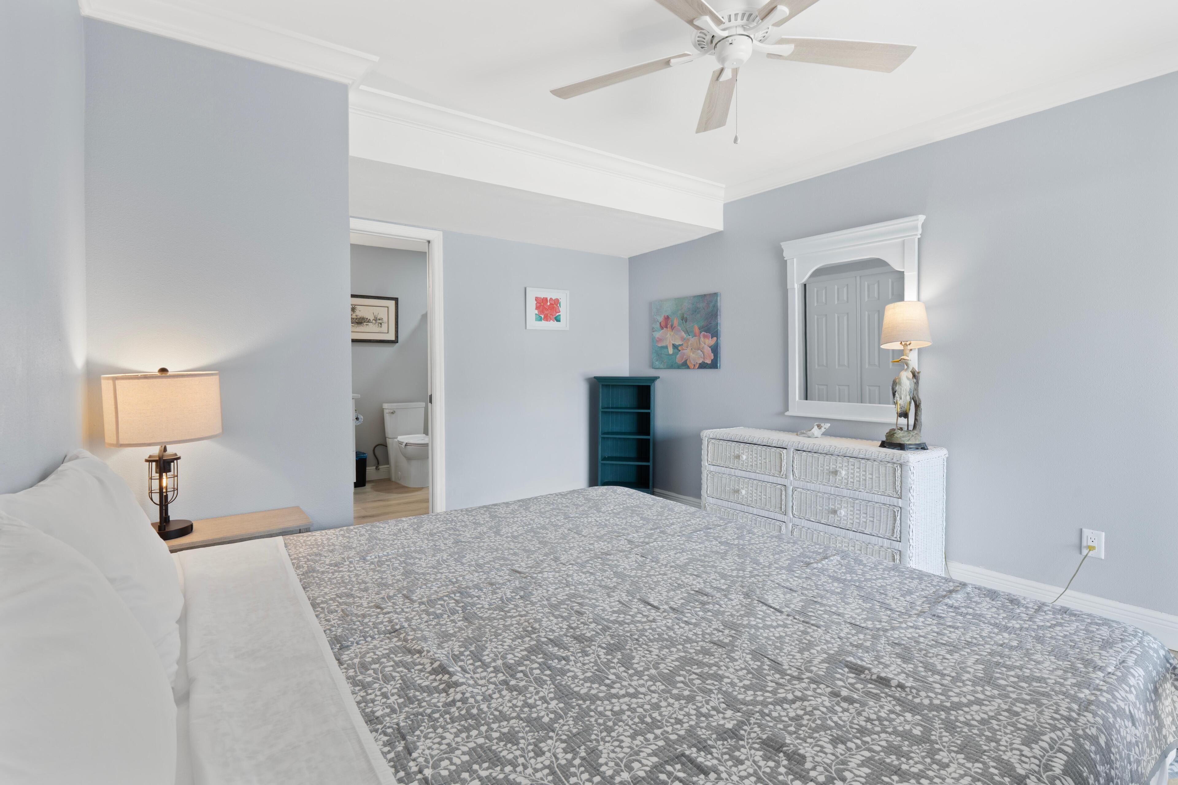 A bedroom with a bed, a dresser, a mirror, and a ceiling fan.