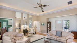Ein geräumiges Wohnzimmer mit zwei beigefarbenen Sofas, einem Glastisch und einem Deckenventilator.
