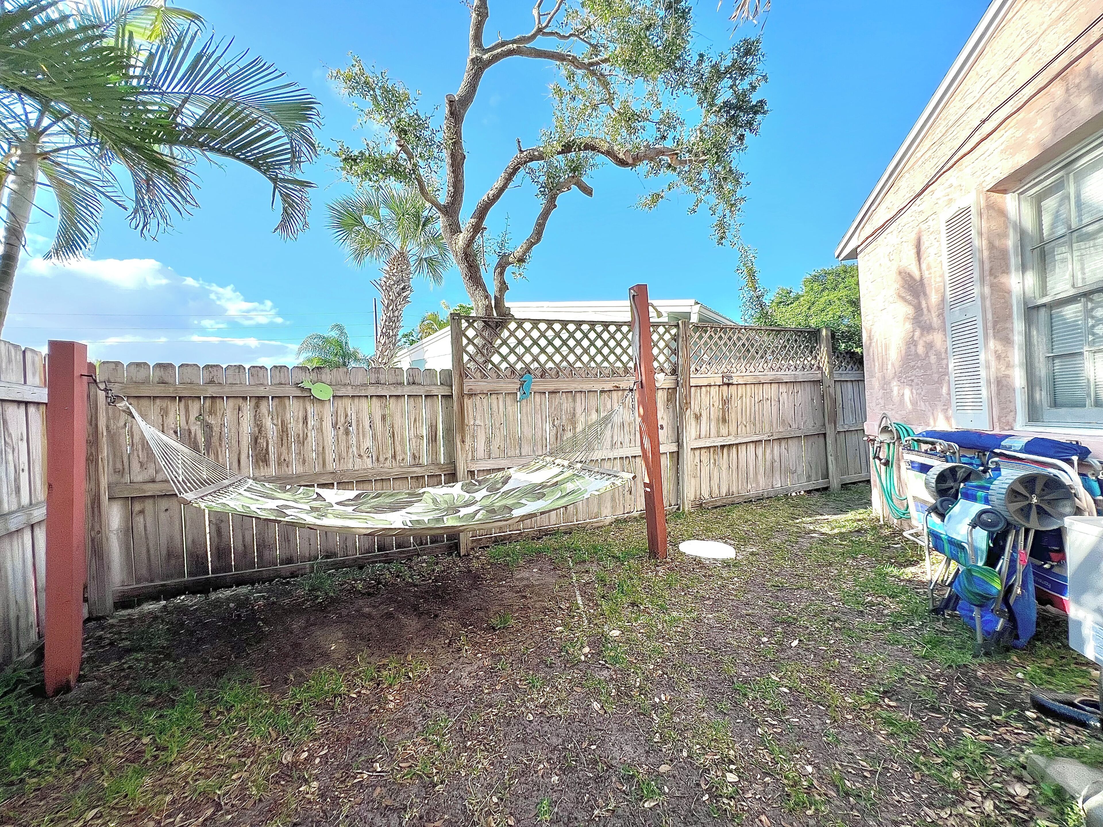 A backyard with a hammock, a wooden fence, and a house.