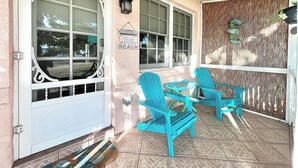 Eine Veranda mit türkisfarbenen Stühlen, einem kleinen Tisch und einem Schild mit der Aufschrift 'Welcome to the Beach'.
