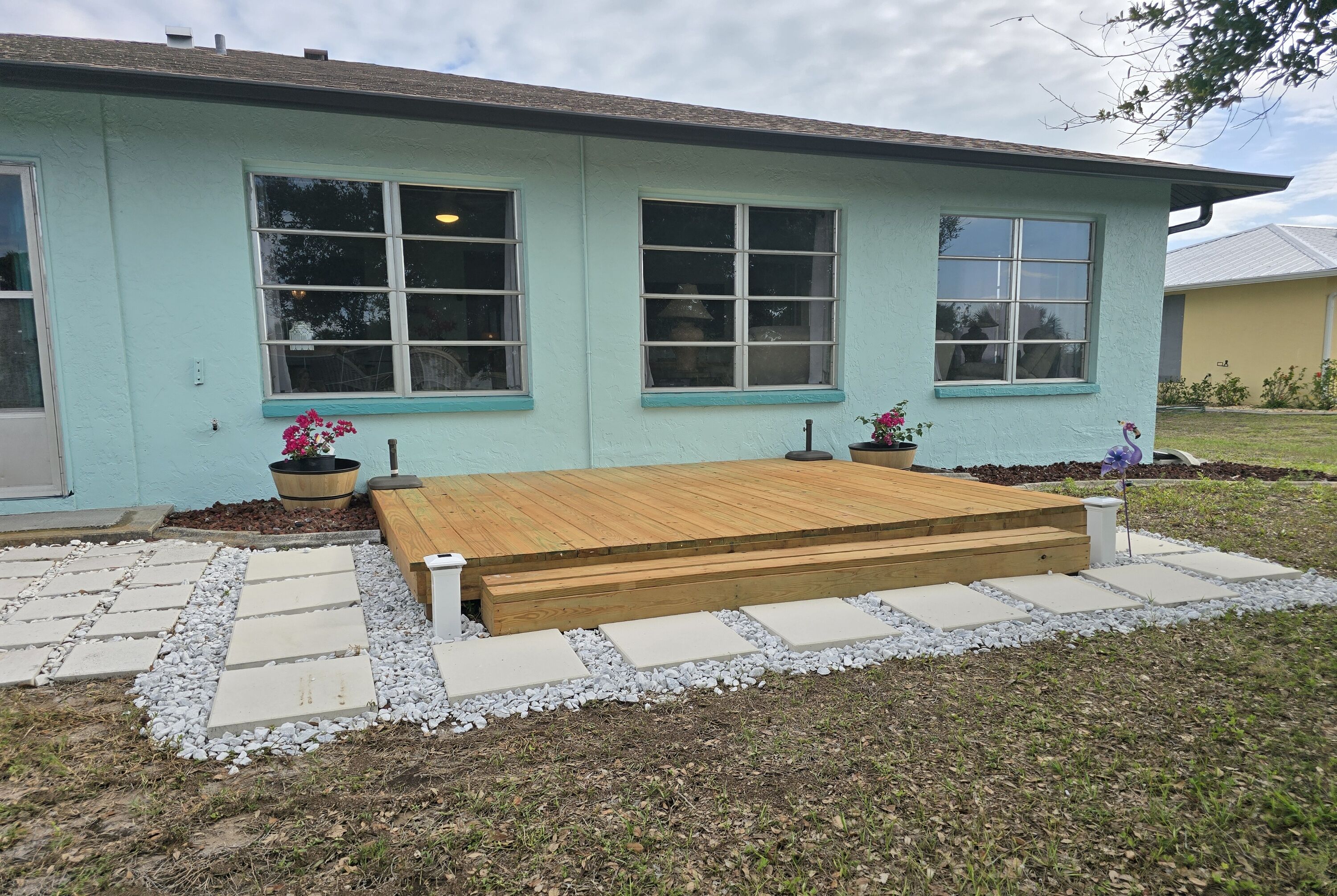 A house with a wooden deck, large windows, and a stone pathway.