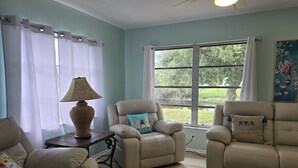 A living room with two beige recliners, a table with a lamp, and a window with curtains. - Spacious 4-bedroom house in charming Rotonda West with WiFi, AC, canal front. (ROTONDA WEST)