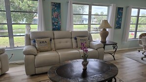 A living room with a beige sofa, a round coffee table with a vase of flowers, and a lamp on a side table. - Spacious 4-bedroom house in charming Rotonda West with WiFi, AC, canal front. (ROTONDA WEST)