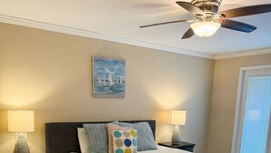 Un dormitorio con una cama grande, dos mesitas de noche, un ventilador de techo y un cuadro en la pared.