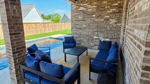 An outdoor patio with brick walls, a pool, and blue outdoor furniture. - Experience the gold standard of Ocean Springs. Private 3BR home with a personal touch you won't find in hotels. Space, style, and local soul. (Ocean Springs)