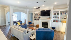 A spacious living room with a fireplace, a television mounted on the wall, and a bookshelf filled with books. - Experience the gold standard of Ocean Springs. Private 3BR home with a personal touch you won't find in hotels. Space, style, and local soul. (Ocean Springs)