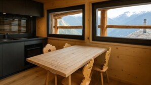 A wooden interior with a kitchen, dining table, and chairs, large windows with mountain views. - Les Mayens d'Adrien (Mase)