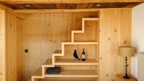 A wooden interior with a staircase, a bird sculpture, a bottle of wine, and a lamp on a nightstand. - Les Mayens d'Adrien (Mase)